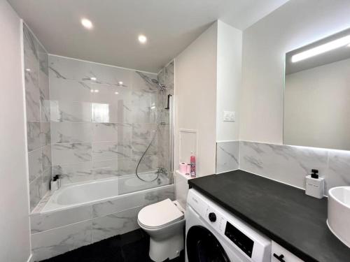 a white bathroom with a tub and a toilet and a sink at Le P'tit Montreuillois - Appartement proche Paris in Montreuil
