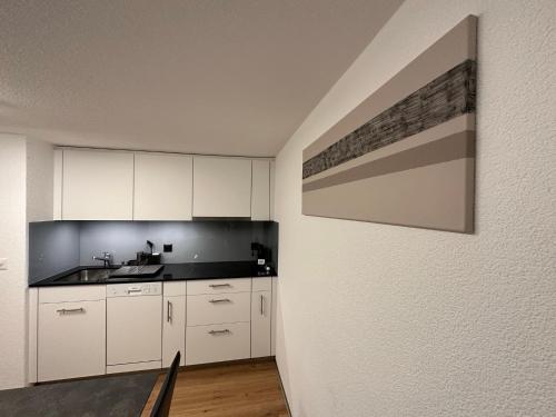 a kitchen with white cabinets and a painting on the wall at Apartment Enzian in Saas-Grund