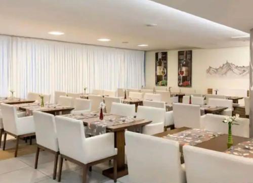 a dining room with wooden tables and white chairs at Macaé Ramada Flat RJ in Macaé
