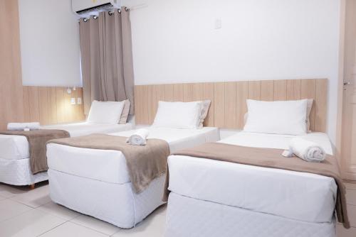 two beds in a hotel room with white furniture at Pousada Areia do Forte in Cabo Frio