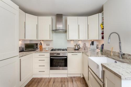 una cocina con armarios blancos y electrodomésticos de acero inoxidable en Chic 3BD Maisonette wRoof Terrace - Wandsworth!, en Londres