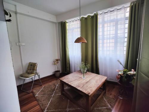 ein Wohnzimmer mit einem Holztisch und grünen Vorhängen in der Unterkunft Ivory Botanic Stay in Darjeeling