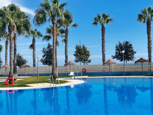 una piscina con palmeras y una valla en Luxurious Spacious Three Bedroom Apartment On Beachfront, en Almerimar