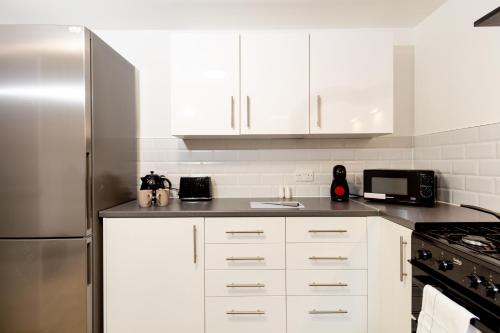 a kitchen with white cabinets and a stainless steel refrigerator at Suite 5 - Stylist Spot in Oldham City Centre in Oldham