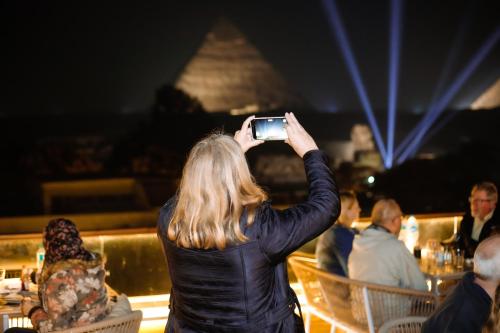 a woman taking a picture of a restaurant with her cell phone at Tree Lounge Pyramids View INN , Sphinx Giza in Cairo