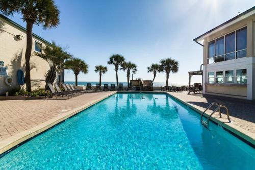 a swimming pool in front of a building with palm trees at Oceanfront Views, Private Porch, 1st Flr, King Bed in Pawleys Island