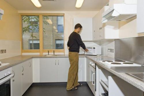 a man standing in a kitchen looking at a microwave at James Lighthill House, Finsbury, London in London