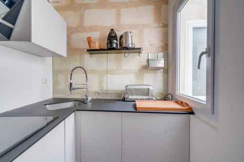 uma cozinha com armários brancos, um lavatório e uma janela em Charming apartment in the heart of Bordeaux em Bordeaux