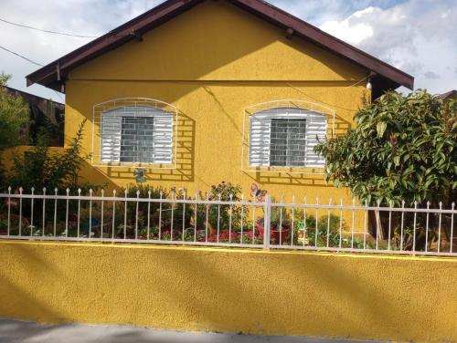una casa amarilla con una valla delante de ella en Simples e confortável en Londrina