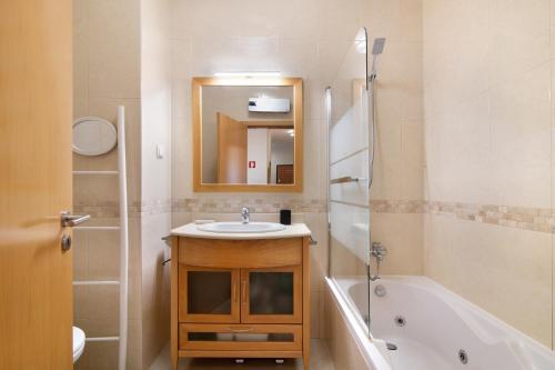 y baño con lavabo, bañera y espejo. en Apartamento da Ourada Marina luz, en Albufeira