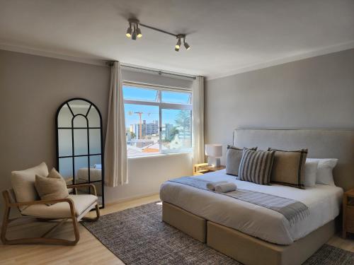a bedroom with a bed and a chair and a window at Sandy Lodge 201 in Cape Town