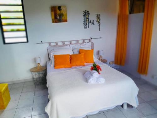 Una cama blanca con almohadas naranjas y flores. en Coconing logements studios et maisons, en Sainte-Anne