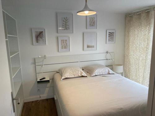 - une chambre blanche avec un lit et des photos sur le mur dans l'établissement Cosy's Terrasse, à Larmor-Plage