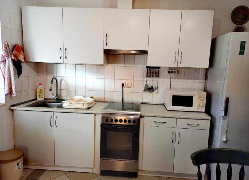 a kitchen with white cabinets and a stove and a microwave at Flower Tisza Vendégház in Tiszafüred