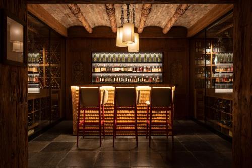 a bar with four chairs in a room with wine bottles at The Alpina Gstaad in Gstaad
