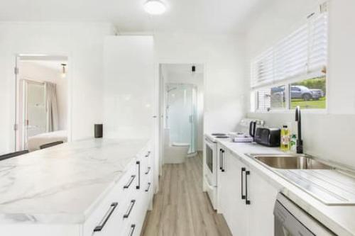 een witte keuken met witte werkbladen en een wastafel bij Cockle Bay Getaway is close to beach in Auckland
