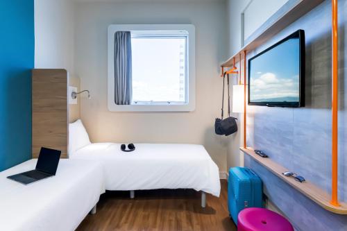 a room with two beds and a window and a laptop at ibis budget Pindamonhangaba in Pindamonhangaba