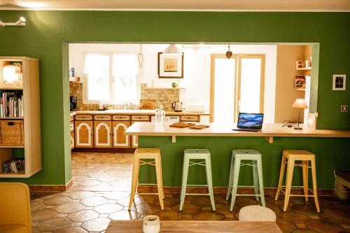 a kitchen with green walls and a counter with stools at La maison du Diplo : Forêt, sentiers et grimpe in Le Vaudoué