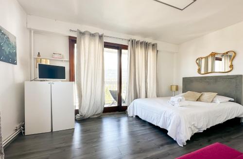 a white bedroom with a bed and a television at Mont Royal balcon et piscine in Annecy