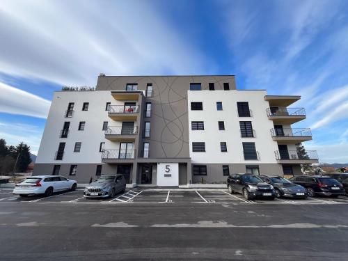 un grand bâtiment blanc avec des voitures garées dans un parking dans l'établissement Felix Celeia Apartment, à Celje