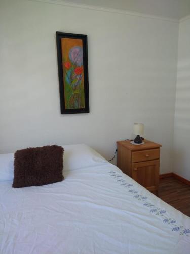 um quarto com uma cama branca e uma fotografia na parede em Alojamiento Ximena em Coñaripe