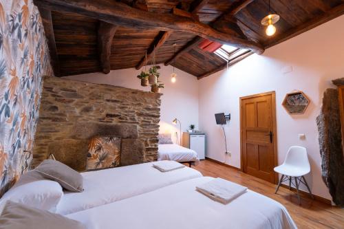 Casa Rural Piñeiro, de Vila Sen Vento في أو بيدروزو: غرفة نوم بسريرين وجدار حجري