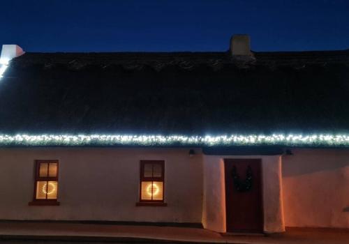 a white house with lights on the roof at night at Luxury 300yr old Irish thatch cottage close to sea in Rush
