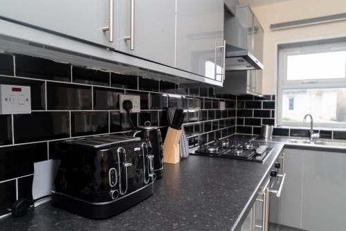 a kitchen with a black and white tiled wall at Beautiful 5 single bedroom house in Dagenham