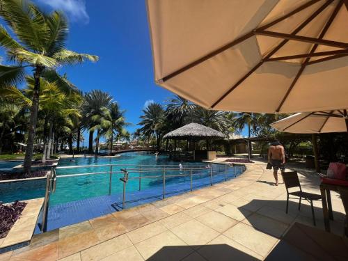 a person walking by a swimming pool with palm trees at Apartamento GolfVille Residence in Aquiraz