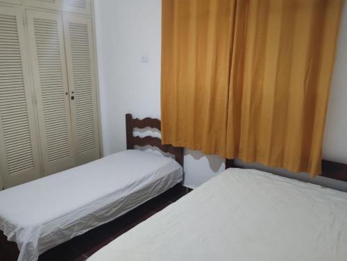 - 2 lits dans une chambre dotée de rideaux jaunes dans l'établissement Casa Harmonia, à Guarujá