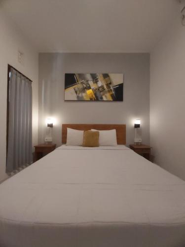 a bedroom with a large white bed with two lamps at Genta House in Kuta
