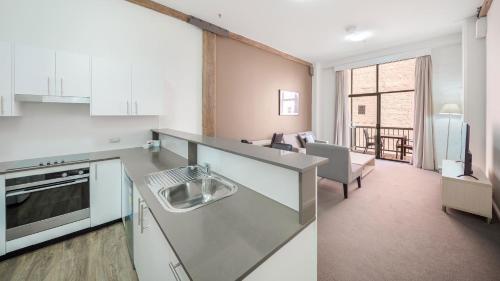 a kitchen with a sink and a living room at Oaks Sydney Goldsbrough Suites in Sydney