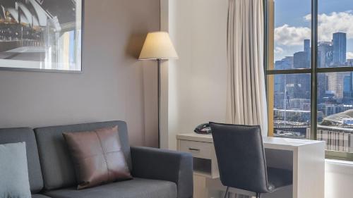 a hotel room with a chair and a desk and a window at Oaks Sydney Goldsbrough Suites in Sydney