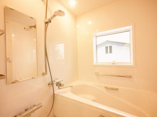 La salle de bains blanche est pourvue d'une baignoire et d'une fenêtre. dans l'établissement 古民家ホテル 結 YUWAI, à Hakuba
