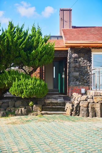 a brick house with a green door and a stone driveway at Hey Day Jeju in Jeju
