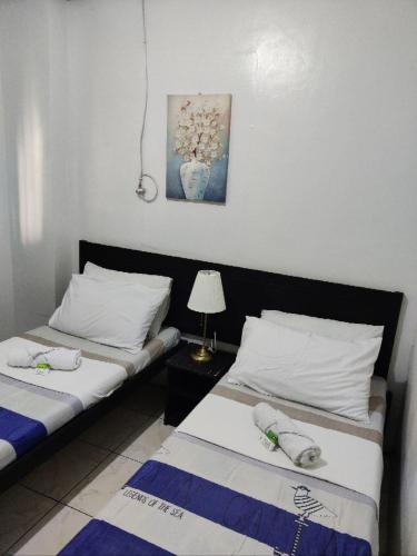 two beds in a room with a lamp on a table at Center Parkway Pension House in Kalibo