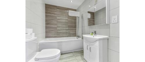 a white bathroom with a toilet and a tub and a sink at Serene Escape: Stylish & Cozy 2BR Flat in London