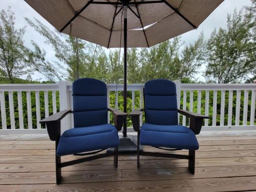 - 2 chaises et une table avec un parasol sur la terrasse couverte dans l'établissement Sheer Bliss BeachView Apt #4, à Exuma Harbour Estates
