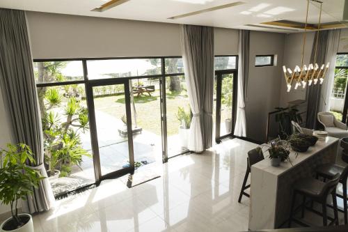 ein Wohnzimmer mit großen Fenstern und Pflanzen in der Unterkunft SHALOM HOUSE _ BẢO LỘC in Bảo Lộc