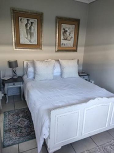 a bedroom with a white bed with two pictures on the wall at Stonehenge Cottage in Oudtshoorn