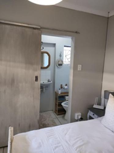 ein Schlafzimmer mit einem Bett und ein Badezimmer mit einem Waschbecken in der Unterkunft Stonehenge Cottage in Oudtshoorn