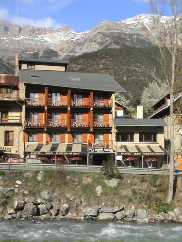 un edificio de hotel con un río frente a una montaña en Chambre Quadruple avec Salle de Bains Privative 1 en Vallouise