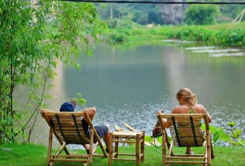 twee mensen in ligstoelen bij een meer bij Quoc Khanh Bamboo Homestay in Ninh Binh