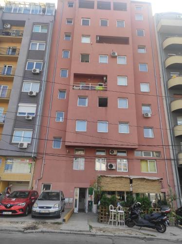 un bâtiment rose avec des voitures garées devant lui dans l'établissement HI Youth and Business Apartments, à Belgrade