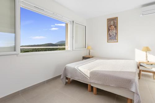 a white bedroom with a bed and a large window at Villa vue mer proche du centre in La Croix-Valmer