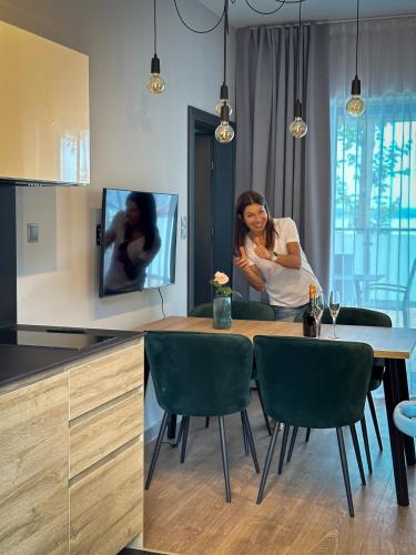 a woman sitting at a table in a kitchen at Lago Apartamenty Domki in Niesulice