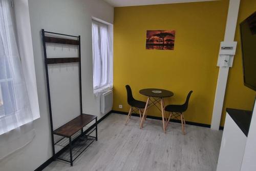 Cette chambre est dotée d'une table, de chaises et d'un mur jaune. dans l'établissement Studio Orchidée, tout confort, rénové, à Saint-Quentin