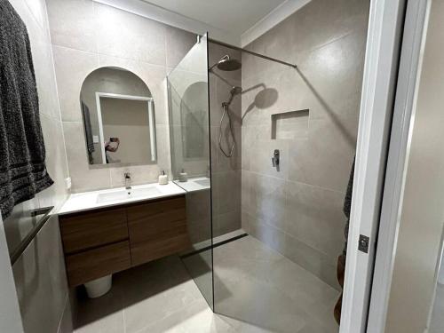 een badkamer met een douche, een wastafel en een spiegel bij Beachside Modern Cedar Home in Emu Park