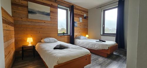 two beds in a room with wooden walls and windows at "Petit Durbuy" by Phils Cottages in Durbuy
