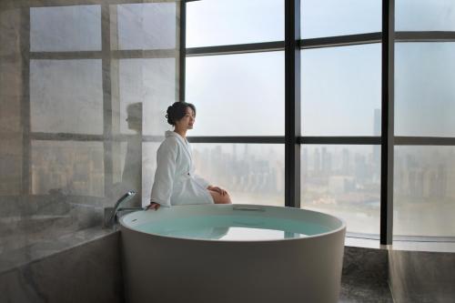 a woman sitting in a bath tub in front of a window at Wuhan Marriott Hotel Wuchang in Wuhan